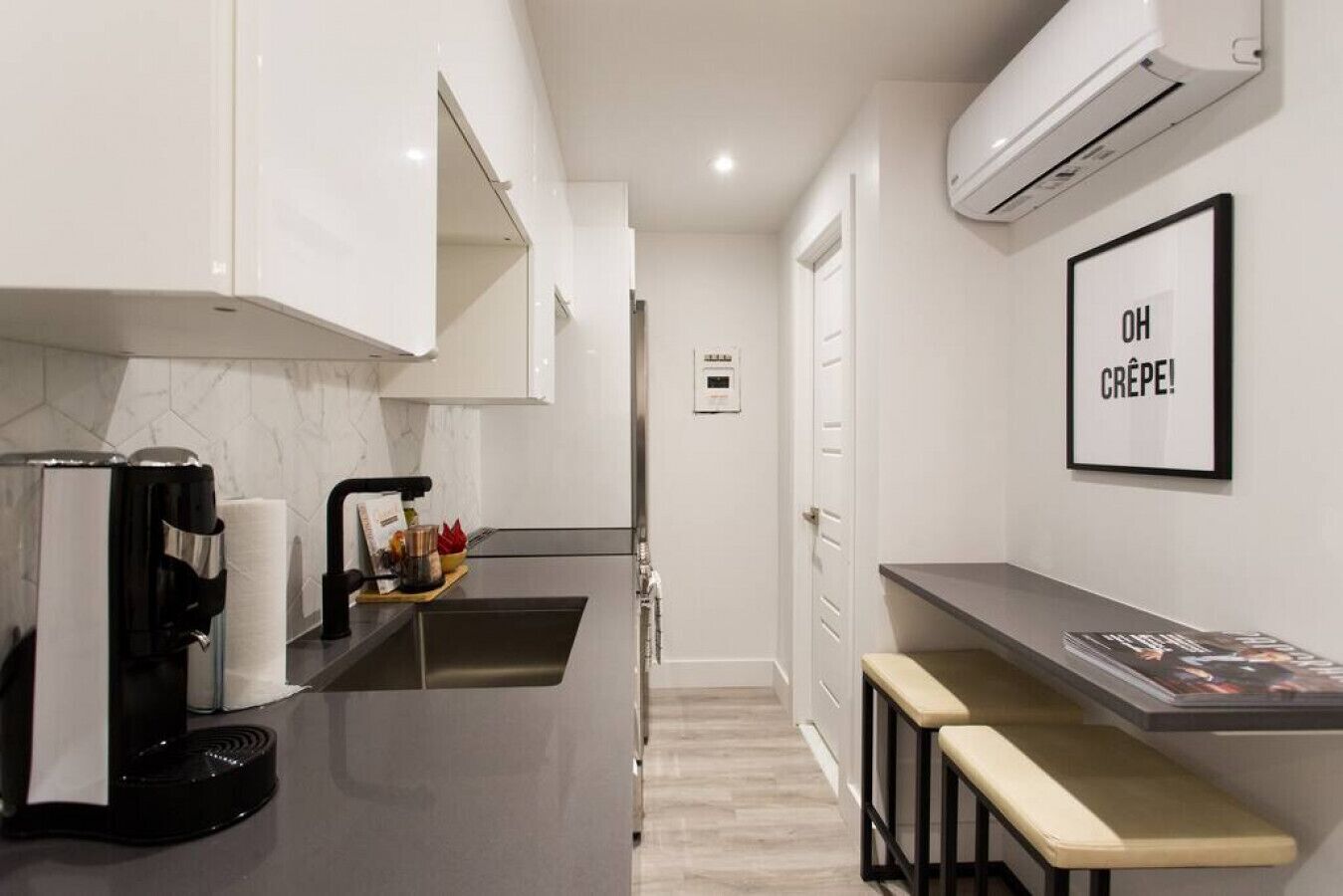 A modern kitchen with a coffee machine, a sink, and a bar area with stools.