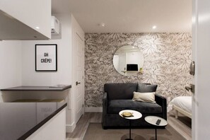 A modern hotel room with a black sofa, a small round table, a mirror, and a framed picture on the wall. - 6768 - 102 · Cozy and Fresh Mini Studio with kitchen  by Denstays (Montréal)
