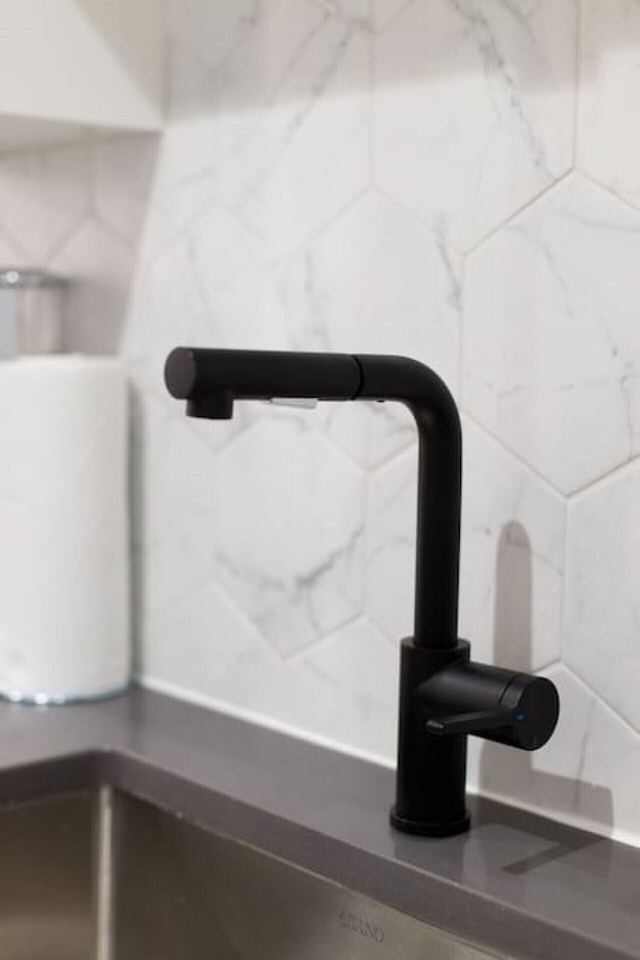 A modern kitchen with a black faucet, white marble backsplash, and a stainless steel sink.