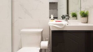 A modern bathroom with a toilet, a sink, a mirror, and a shower area.