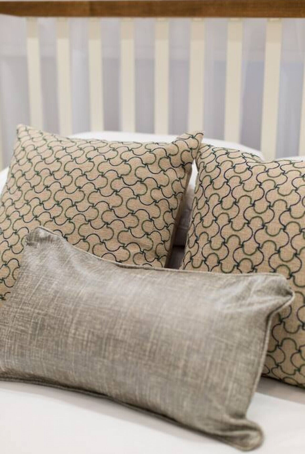 A bed with striped wallpaper, two patterned pillows, and a plain pillow.