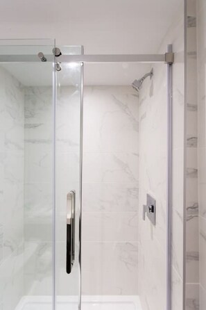 Een douche met glazen wanden, een marmeren muur en een metalen handgreep.