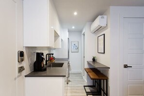 A narrow kitchen with white cabinets, a coffee machine, a sink, and a bench.