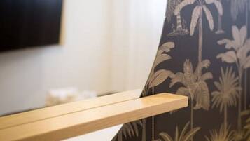 A bathroom with a mirror, a wooden shelf, and a wall with palm tree wallpaper.
