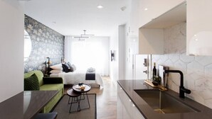 Ein modernes Hotelzimmer mit Bett, einem grünen Sofa, einem kleinen Tisch und einer Küchenzeile inklusive Spüle und Arbeitsplatte.