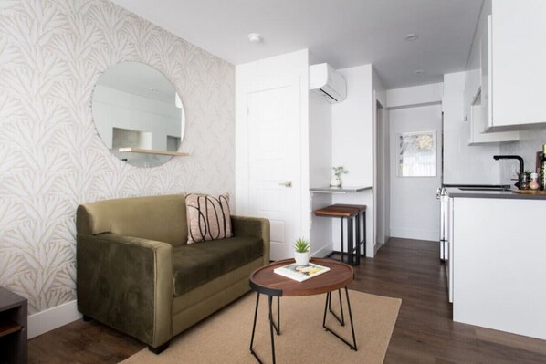 Una sala de estar moderna con un sofá, una mesa redonda de centro y una zona de cocina con encimera y armarios.