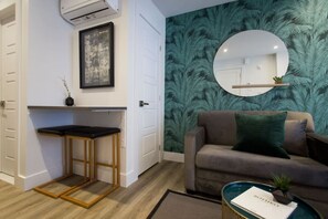 Una sala moderna con un sofá gris, un espejo redondo y una pequeña mesa con una planta.