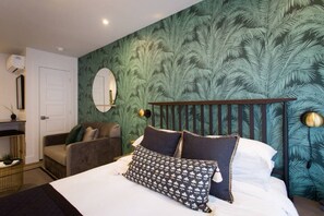 Un dormitorio con una cama, una mesita de noche, un tocador, un espejo y una pared con motivos de hojas.