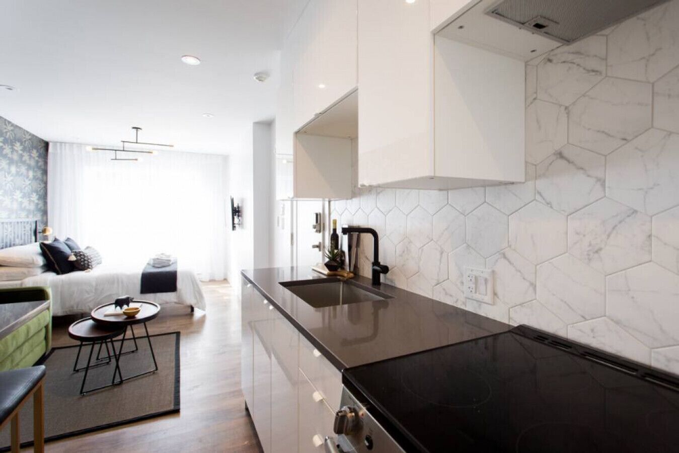 A modern kitchen with a black countertop, a hexagonal tile backsplash, and a visible stove. - 6768 - 203 · Golden Oasis mini Studio with full bath  by Denstays (Montréal)