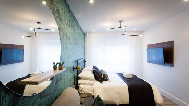 A modern hotel room with two beds, a large mirror, a TV, and a unique green wall feature. - 6768 - 203 · Golden Oasis mini Studio with full bath  by Denstays (Montréal)
