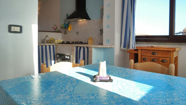 Una cocina con mantel azul estampado, una silla de madera y una ventana con cortinas.