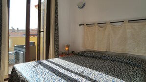 Un dormitorio con cama, mesita de noche, lámpara, ventana con cortinas y vistas al exterior.