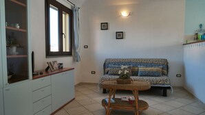 Una habitación con un sofá, una mesa de mimbre y un mueble con vajilla.