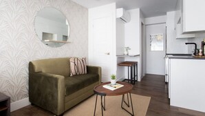 Una sala de estar moderna con un sofá, una mesa redonda de centro y una zona de cocina con encimera y armarios.