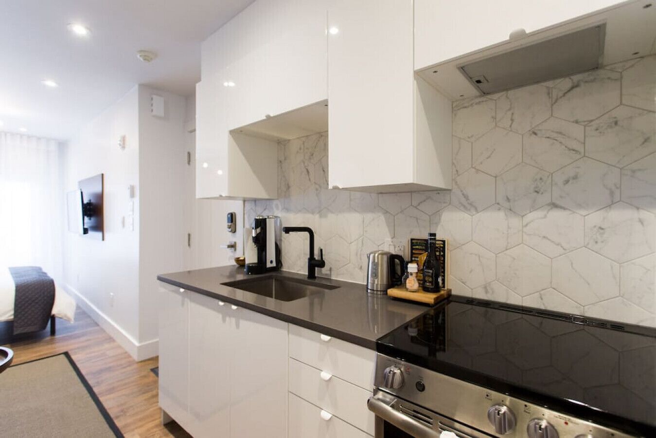 Une cuisine moderne avec des meubles blancs, un plan de travail noir, une cuisinière en acier inoxydable et un dosseret de carrelage hexagonal.