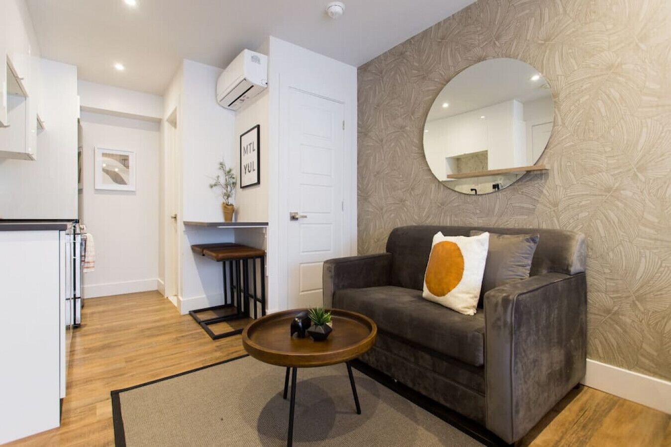 Un espace de vie compact comprenant un canapé, une table basse, un miroir et un coin cuisine.