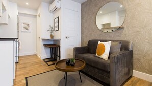 Un espacio habitable compacto con sofá, una mesita de centro, un espejo y una zona de cocina.