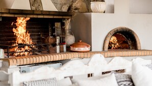 A brick fireplace with a fire, a stone oven, and a white cushioned seating area. - Casa Della Vita (Hersonissos)