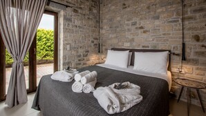 A bedroom with a stone wall, a bed with white linens, a small round table, and a curtain. - Casa Della Vita (Hersonissos)