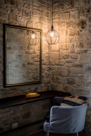A stone wall with a framed mirror and two hanging light fixtures.