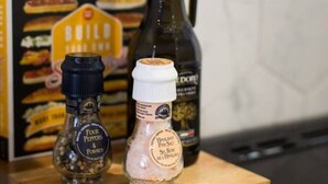 Una encimera de cocina con una tabla de cortar de madera que sostiene tres botellas: una botella oscura con tapa negra, una botella blanca con tapa blanca y una botella transparente con tapa negra.