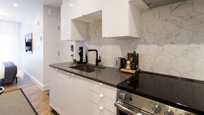 Una cocina moderna con gabinetes blancos, encimera negra, estufa de acero inoxidable y salpicadero de azulejos hexagonales.
