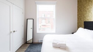 Een hotelkamer met een bed, een kledingkast, een spiegel en een raam met uitzicht op gebouwen.