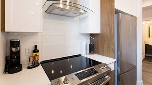 A modern kitchen with a built-in stove, a coffee maker, and a refrigerator. - Brand New Light filled Mile End Flat by Denstays (Montréal)