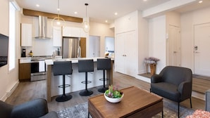 A modern kitchen with a central island, bar stools, and a dining area with a coffee table. - Brand New Light filled Mile End Flat by Denstays (Montréal)