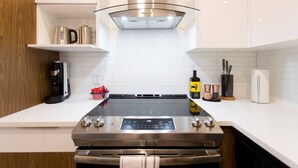 Una cocina moderna con estufa de acero inoxidable, campana de vidrio, armarios blancos y cafetera.