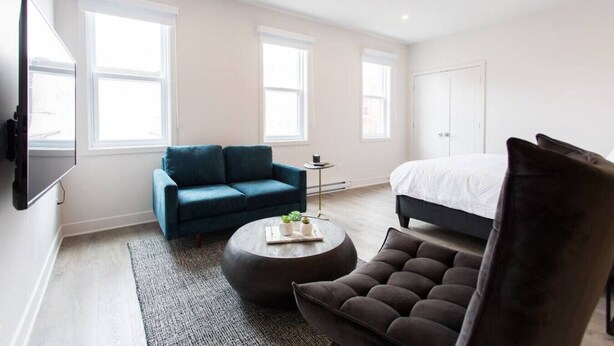 Un dormitorio moderno con un sofá azul oscuro, una mesa de centro redonda, un sillón oscuro y una cama grande.