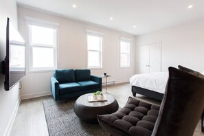 A modern bedroom with a dark blue sofa, a round coffee table, a dark armchair, and a large bed. - Live Like a Local in this Superb Loft by Denstays (Montréal)