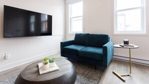 Una sala de estar moderna con un sofá azul verdoso, una mesa redonda de centro con objetos decorativos, una mesita auxiliar con una taza y un televisor montado en la pared.