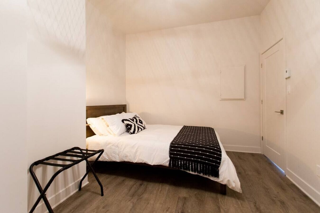 A small, neatly arranged bedroom with a bed, a bedside table, and a door.