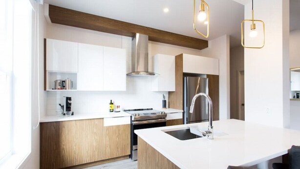 A modern kitchen with white cabinetry, a stainless steel range, a central island with a sink, and pendant lighting. - Huge 2 Bdr with Balcony in Mile End by Denstays (Montréal)