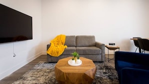 A living room with a grey sofa, a wooden coffee table, a blue armchair, a flat-screen TV mounted on the wall, and a small side table with a book. - Huge 2 Bdr with Balcony in Mile End by Denstays (Montréal)