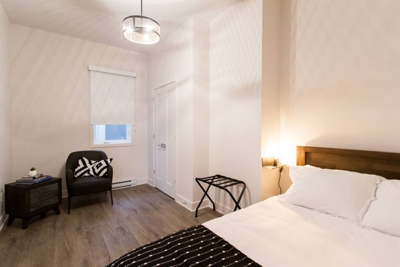 A bedroom with a bed, a chair, a small table, a window, and a door.