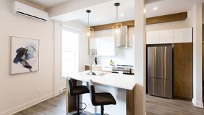 A modern kitchen with a central island, bar stools, stainless steel appliances, and a hanging light fixture. - Huge 2 Bdr with Balcony in Mile End by Denstays (Montréal)