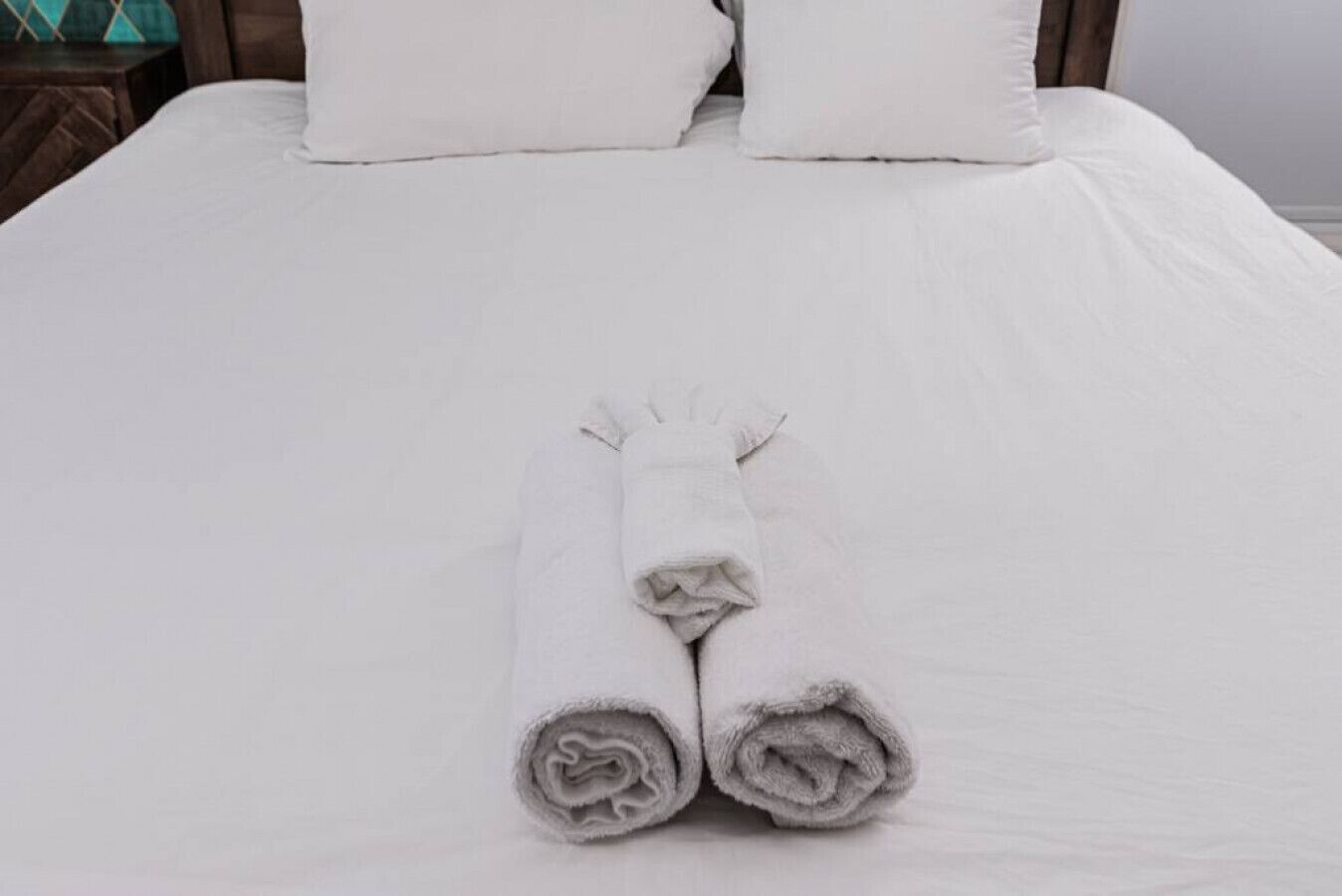 Una cama bien hecha con sábanas blancas y dos toallas enrolladas sobre ella.