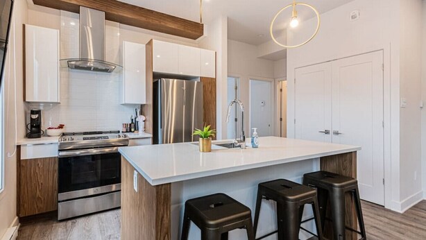 Une cuisine moderne dotée d’un îlot central, d’appareils électroménagers en acier inoxydable et d’éléments décoratifs en bois.