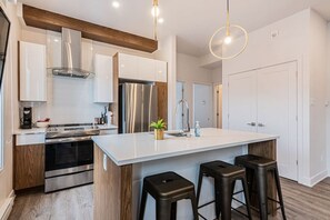 Une cuisine moderne dotée d’un îlot central, d’appareils électroménagers en acier inoxydable et d’éléments décoratifs en bois.