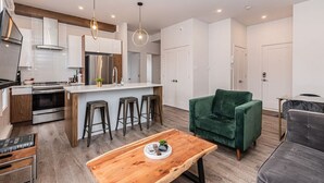 Une cuisine moderne avec un îlot central, des tabourets de bar, un canapé en velours vert et une table basse en bois.
