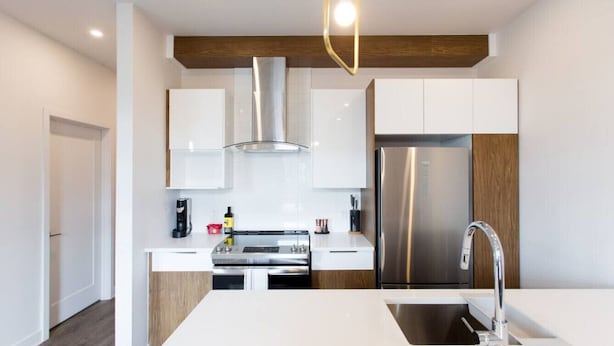 A modern kitchen with white cabinetry, stainless steel appliances, and a central island with a sink. - Light Filled 2 Bdr Unit in Mile End by Denstays (Montréal)