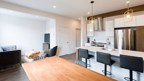 A modern kitchen with a central island, bar stools, and a wooden dining table. - Light Filled 2 Bdr Unit in Mile End by Denstays (Montréal)