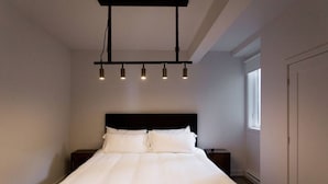 A bedroom with a bed, a nightstand, a hanging light fixture, and a window. - Light Filled 2 Bdr Unit in Mile End by Denstays (Montréal)