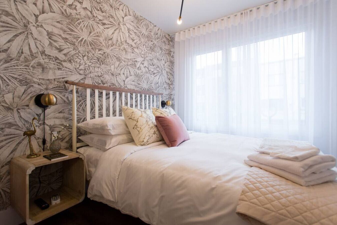 A bedroom with a bed, a bedside table, a lamp, and a window with curtains.