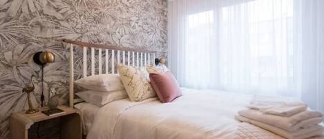 A bedroom with a bed, a bedside table, a lamp, and a window with curtains.