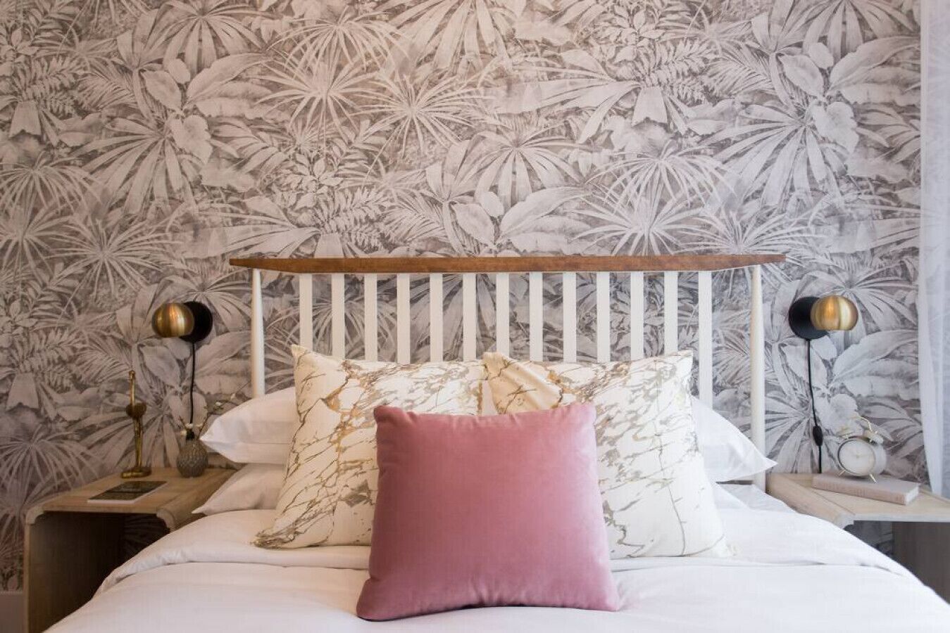 Una cama con ropa de cama blanca, un cabecero de madera y un estampado floral en el papel tapiz.