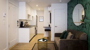 Un apartamento moderno con cocina, sala de estar con sofá, espejo redondo y una pequeña mesita con planta.