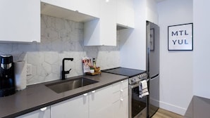 Una cocina moderna con encimera negra, electrodomésticos de acero inoxidable y un salpicadero de azulejos hexagonales.